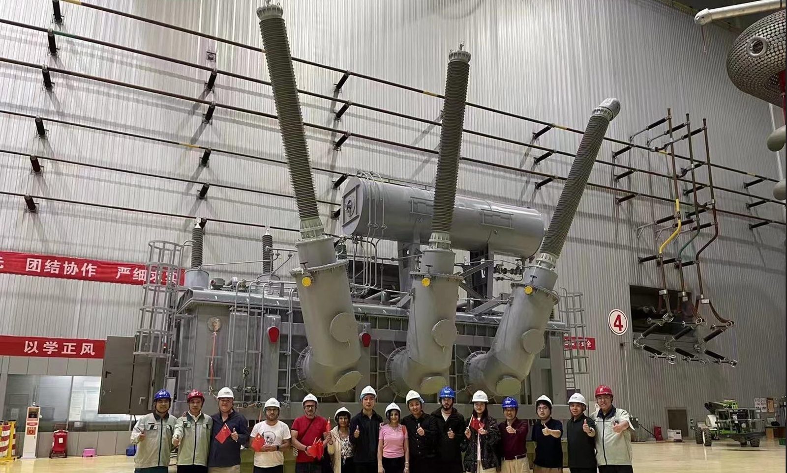 A high-voltage transformer with three bushings in a test hall, with an engineering team standing in front for scale