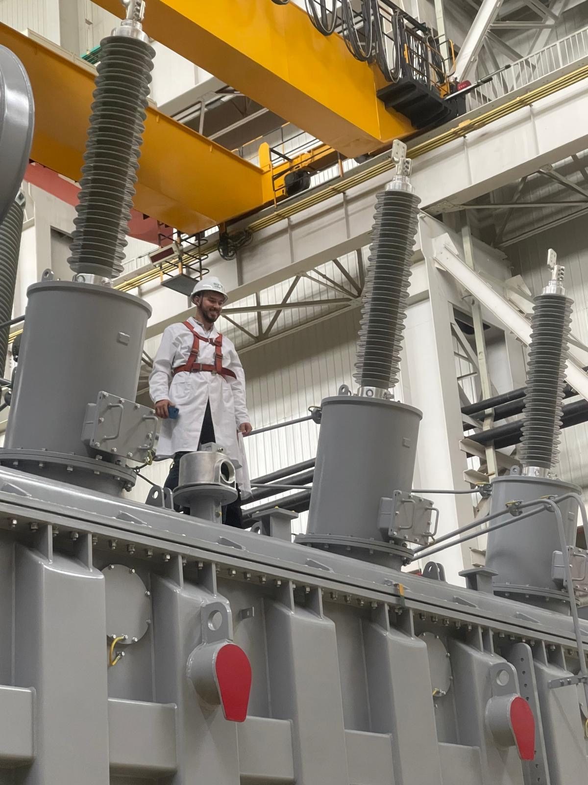 An engineer on top of a power transformer beside its high-voltage bushings